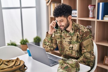 Young arab man army soldier using laptop talking on the smartphone at home