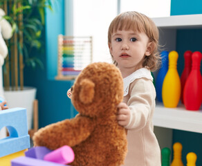 Adorable hispanic girl holding doll standing at kindergarten