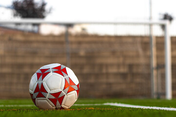 Soccer ball on the grass in front of the field. View from the ground of a soccer ball in front of the field. View of a soccer ball on the grass with a field in the background © Ivi - Powerlightss