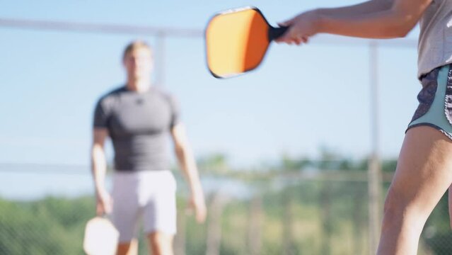 couple playing pickleball game, hitting pickleball yellow ball with paddle, outdoor sport leisure activity.