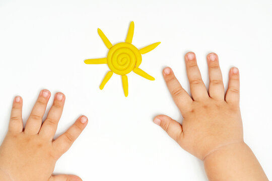 Baby hands and yellow sun of plasticine on white background.