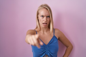 Young caucasian woman standing over pink background pointing displeased and frustrated to the...