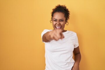 Young hispanic woman with curly hair standing over yellow background pointing displeased and frustrated to the camera, angry and furious with you