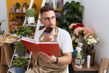 Young hispanic man florist talking on smartphone reading book at flower shop