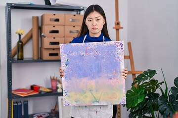 Chinese young woman holding canvas at art studio depressed and worry for distress, crying angry and...