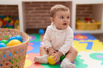 Adorable toddler playing with balls sitting on floor at kindergarten