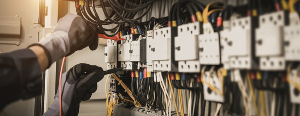 Electricity and electrical maintenance service, Engineer hand holding AC multimeter checking electric current voltage at circuit breaker terminal and cable wiring main power distribution board.