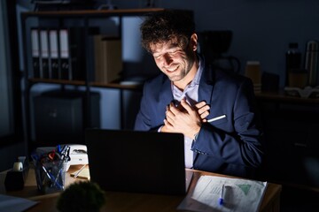 Hispanic young man working at the office at night smiling with hands on chest with closed eyes and grateful gesture on face. health concept.