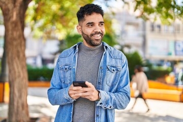 Fototapeta premium Young hispanic man smiling confident using smartphone at park