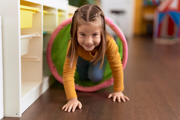 Adorable hispanic girl crawling inside tunnel toy at kindergarten