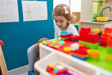 Fototapeta premium Adorable caucasian girl playing with construction blocks standing at kindergarten