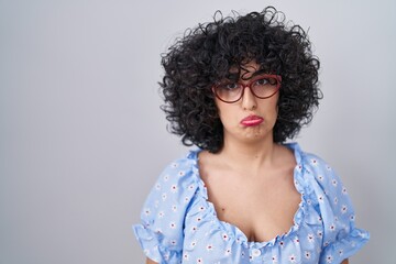 Young brunette woman with curly hair wearing glasses over isolated background depressed and worry for distress, crying angry and afraid. sad expression.