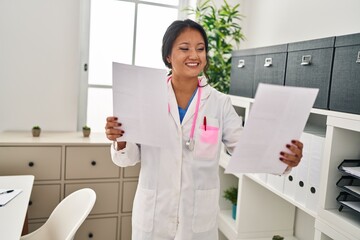 Young chinese woman wearing doctor uniform reading document at clinic