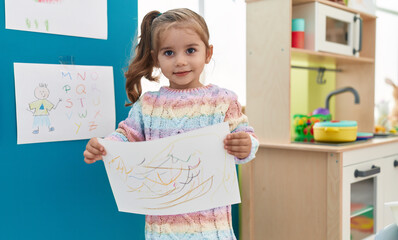Adorable hispanic girl student smiling confident holding draw at kindergarten