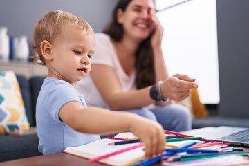 Mother and son sitting on sofa drawing on notebook at home