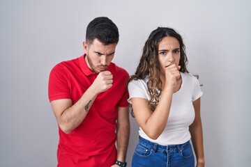 Young hispanic couple standing over isolated background feeling unwell and coughing as symptom for cold or bronchitis. health care concept.