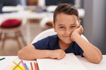 Adorable hispanic toddler student smiling confident sitting on table at classroom