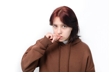 A teenage girl is sad on a light background, she is biting her fingernails, she is very nervous, she is worried about studying in senior classes at school, girl has problems with communication