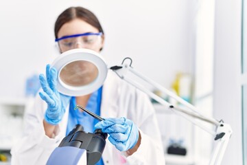 Young hispanic woman wearing scientist uniform analysing insect at laboratory