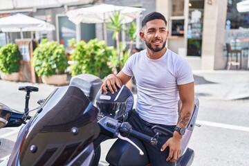 Young latin man holding helmet sitting on motorbike at street
