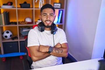 Young latin man streamer smiling confident sitting with arms crossed gesture at gaming room