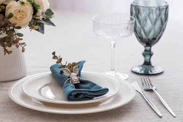 Beautiful spring table setting. A plate with a cotton napkin with a bunny. Silverware and a vase of flowers on a linen tablecloth. The concept of festive serving and a bright Easter holiday.