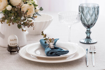 Beautiful spring table setting. A plate with a cotton napkin with a bunny. Silverware and a vase of flowers on a linen tablecloth. The concept of festive serving and a bright Easter holiday.