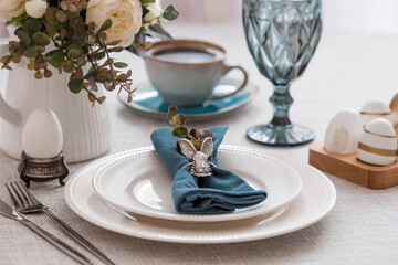Beautiful spring table setting. A plate with a cotton napkin with a bunny. Silverware and a vase of flowers on a linen tablecloth. The concept of festive serving and a bright Easter holiday.