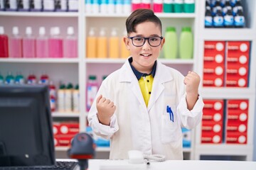 Young hispanic kid working at pharmacy drugstore celebrating surprised and amazed for success with arms raised and eyes closed