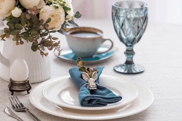 Beautiful spring table setting. A plate with a cotton napkin with a bunny. Silverware and a vase of flowers on a linen tablecloth. The concept of festive serving and a bright Easter holiday.