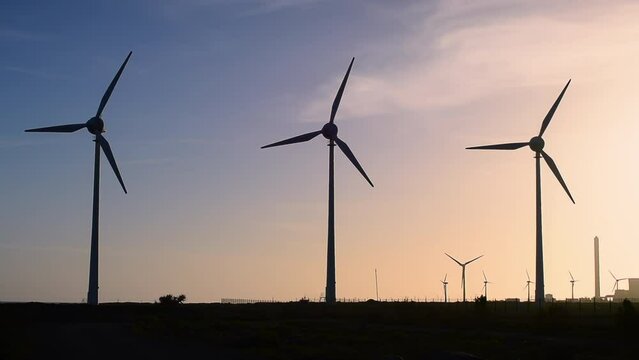 Wind turbines generate electricity, windmill silhouettes at sunset