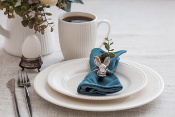 Beautiful spring table setting. A plate with a cotton napkin with a bunny. Silverware and a vase of flowers on a linen tablecloth. The concept of festive serving and a bright Easter holiday.