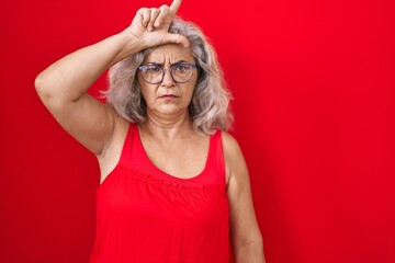 Middle age woman with grey hair standing over red background making fun of people with fingers on...