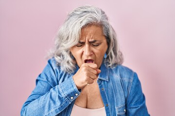 Middle age woman with grey hair standing over pink background feeling unwell and coughing as symptom for cold or bronchitis. health care concept.