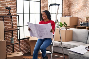 Young african american with braids standing on new home looking at blueprints winking looking at...