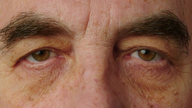 Thick eyebrows in an elderly man close-up. The face and eyes of an old man. Large wrinkles on the face of an elderly man. Face close up. A senior citizen looks into camera