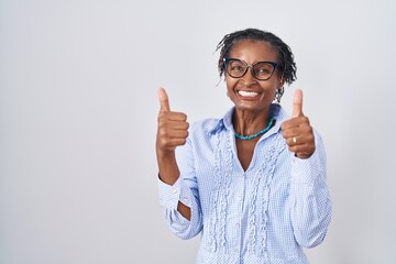 African woman with dreadlocks standing over white background wearing glasses success sign doing...