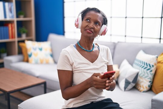 Middle age african american woman listening to music sitting on sofa at home