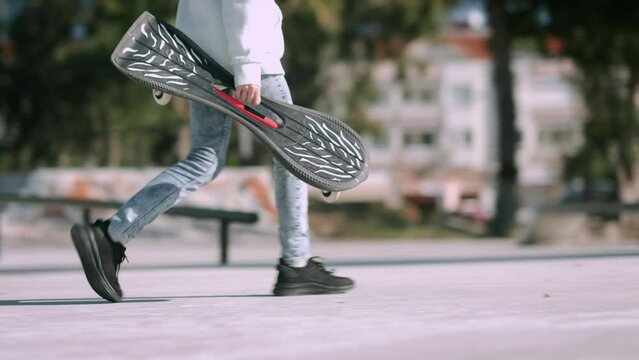 Girl walking with waveboard two wheels in skatepark, modern street skate sports of teenagers, casterboard or ripstick for balance ride.