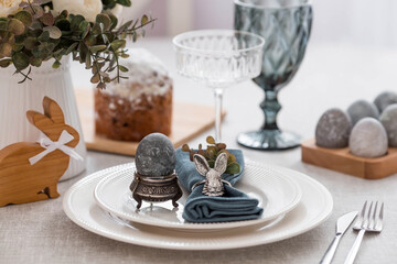 Spring table setting. A plate with a cotton napkin with a bunny, a cake and Easter eggs. Silverware, Easter bunnies and a vase of flowers on a linen tablecloth. The concept of a bright Easter holiday.