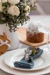 Spring table setting. A plate with a cotton napkin with a bunny, a cake and Easter eggs. Silverware, Easter bunnies and a vase of flowers on a linen tablecloth. The concept of a bright Easter holiday.