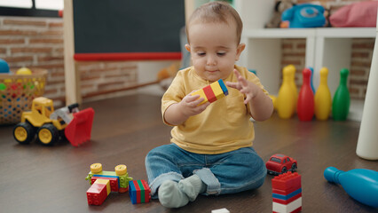 Adorable hispanic baby playing with construction blocks sitting on floor at kindergarten