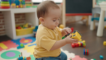 Adorable hispanic baby playing with car toy sitting on floor at kindergarten