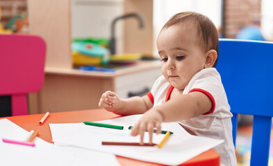 Adorable hispanic baby preschool student sitting on table drawing on notebook at kindergarten
