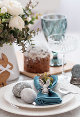Spring table setting. A plate with a cotton napkin with a bunny, a cake and Easter eggs. Silverware, Easter bunnies and a vase of flowers on a linen tablecloth. The concept of a bright Easter holiday.
