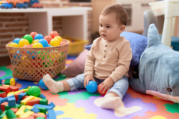 Fototapeta na wymiar Adorable toddler playing with balls sitting on floor at kindergarten