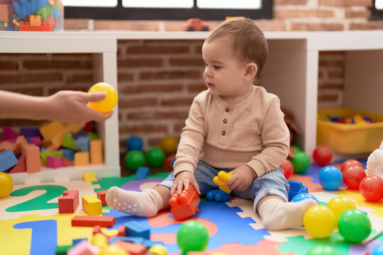 Adorable toddler playing with plastic construction blocks looking ball at kindergarten