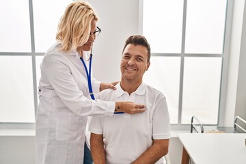 Fototapeta premium Middle age man and woman doctor and patient auscultating heart having medical consultation at clinic