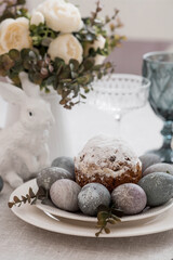 Spring table setting. A plate with a cotton napkin with a bunny, a cake and Easter eggs. Silverware, Easter bunnies and a vase of flowers on a linen tablecloth. The concept of a bright Easter holiday.