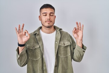 Young hispanic man standing over isolated background relaxed and smiling with eyes closed doing meditation gesture with fingers. yoga concept.